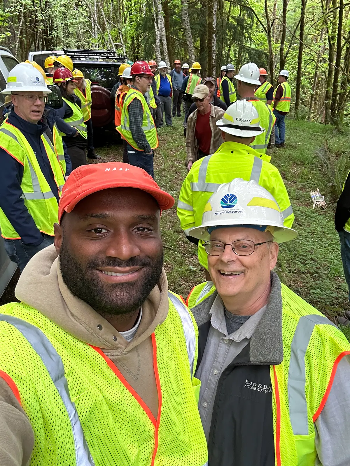 Tour participants in high-visibility vests and hard hats gathered among trees during a Department of Natural Resources field visit